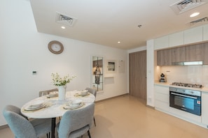 Une cuisine moderne dotée d’un four encastré et d’un coin repas avec une table en marbre et des chaises à revêtement gris.