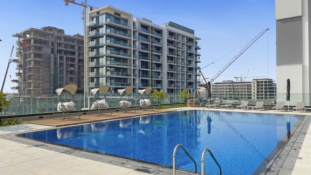 A swimming pool with lounge chairs and a view of a high-rise building under construction. - Brand New 1 BHK in Dubai Hills Estate (Dubai)
