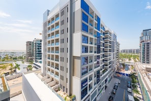 Un edificio residencial de varios pisos con balcones, un jardín en la azotea y un área de estacionamiento.