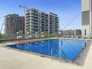 Una piscina con sillones de descanso y vista a un rascacielos en construcción.