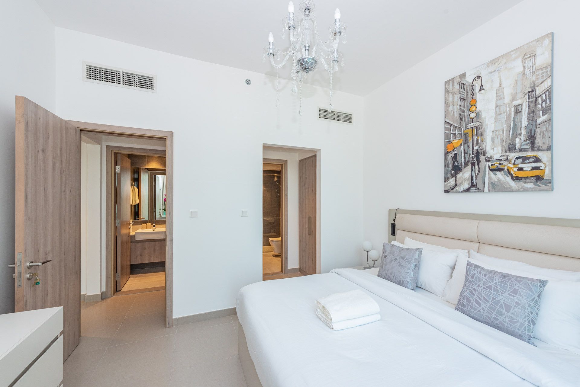 A hotel room with a bed, a painting, and a chandelier.