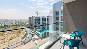Un balcon doté d’une balustrade en verre, qui offre une vue sur un quartier résidentiel moderne avec plusieurs immeubles de grande hauteur et une grue de construction visible au loin.