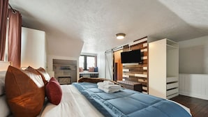 Een slaapkamer met een groot bed, een televisie bevestigd aan een houten wand en een raam met gordijnen.