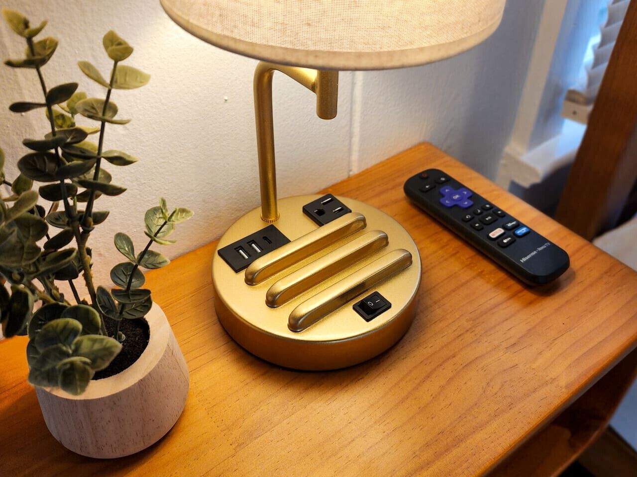 Une table de chevet avec une lampe, une télécommande et une plante en pot.