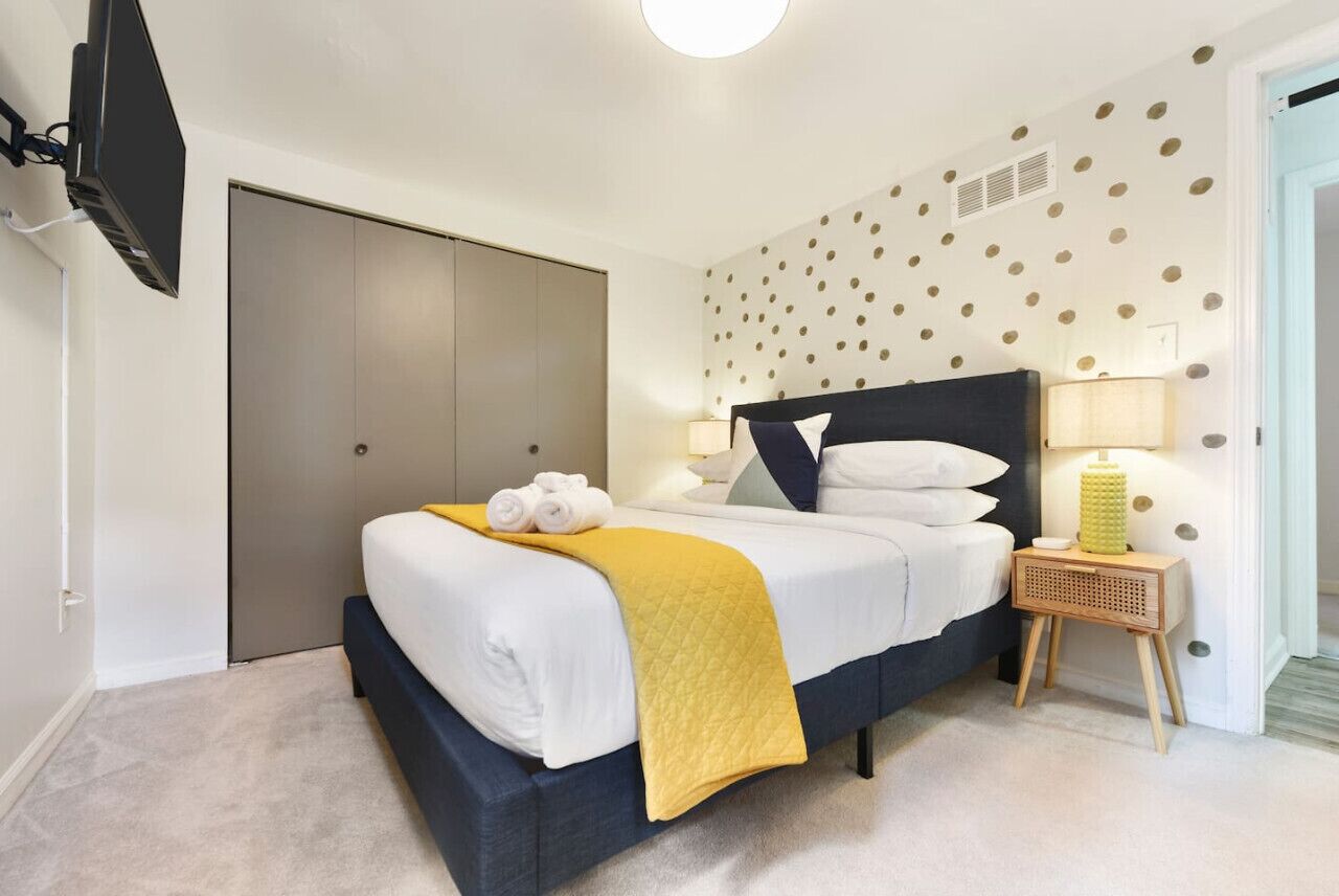 A bedroom with a bed, a bedside table, a wall-mounted TV, and a door.