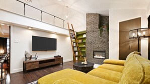 Ein modernes Wohnzimmer mit einem großen Flachbildfernseher, einem Kamin, einem gelben Sofa und einer Holzleiter.