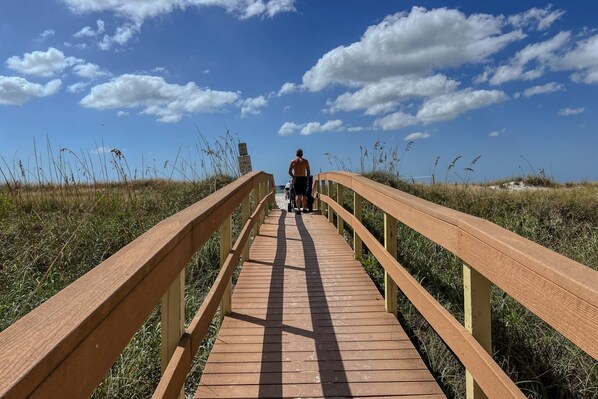 A wooden boardwalk leading to a beach with a clear sky and distant dunes. - Leave Your Worries Behind! Premier Beachfront Resort. Pools, Hot Tubs, Beachfront Tiki Bar, Cafe. (Treasure Island)