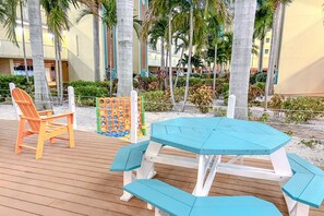 A wooden deck with a turquoise picnic table and an orange Adirondack chair.