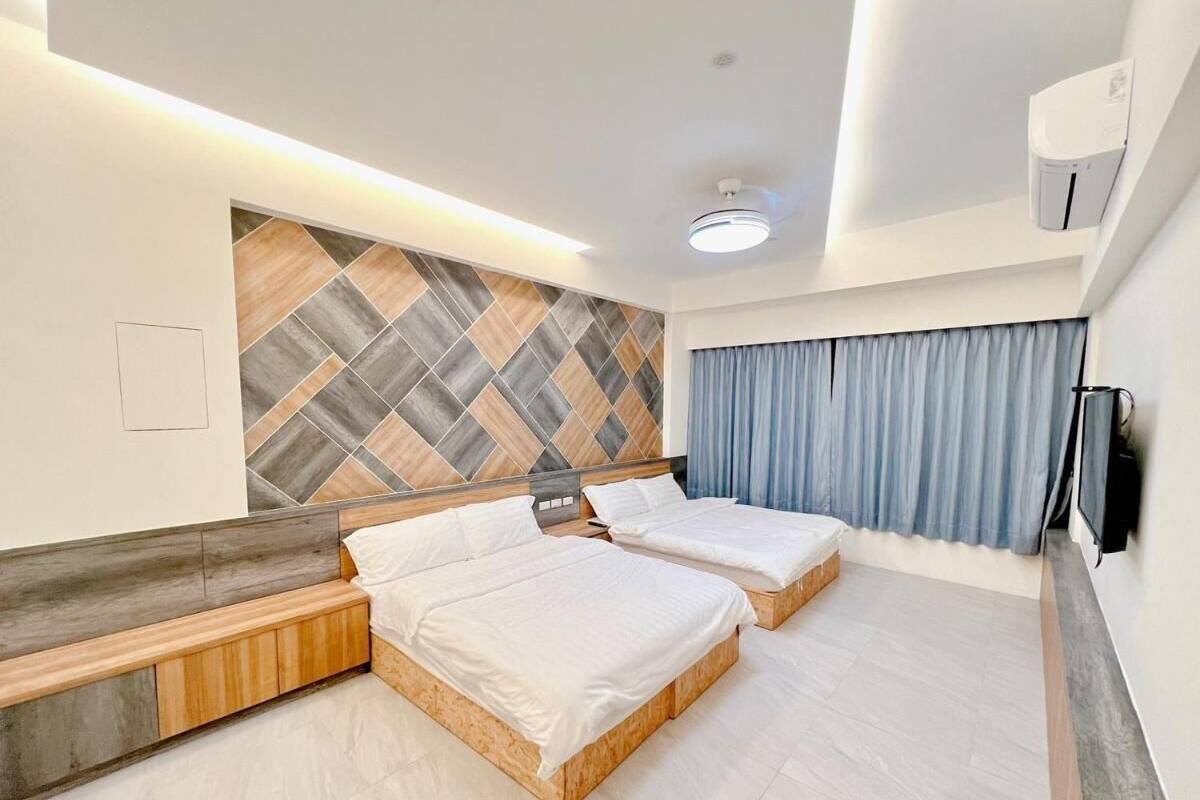 Una habitación de hotel moderna con dos camas, un banco empotrado, un espejo grande y un papel tapiz estampado.