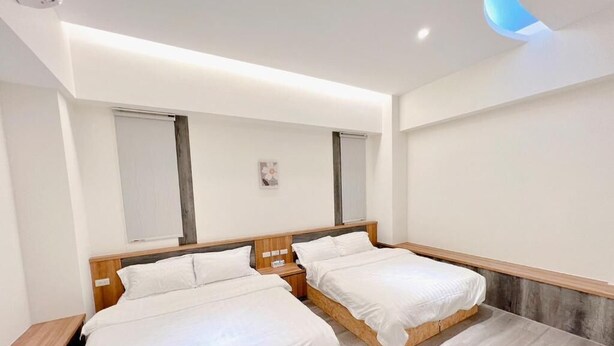 Een moderne hotelkamer met twee eenpersoonsbedden, een houten hoofdbord, een klein nachtkastje en een plafondlamp.