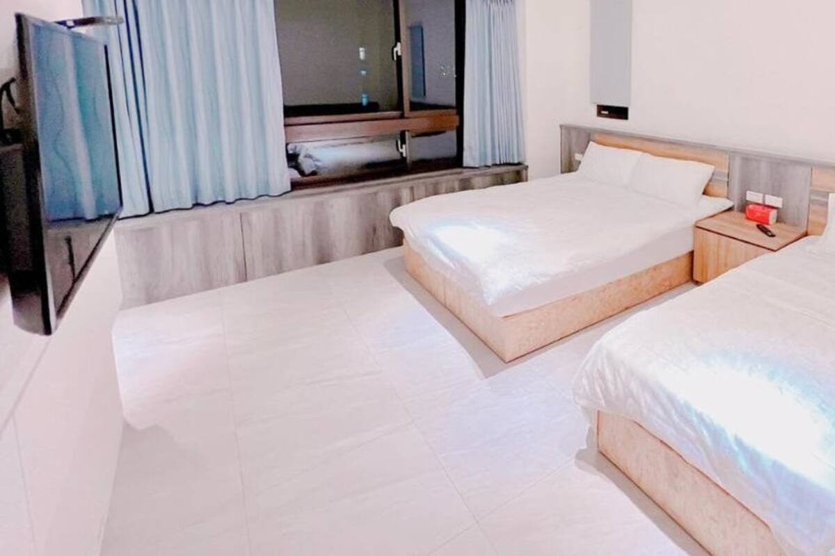 Una habitación de hotel con dos camas individuales, un televisor y una ventana con cortinas.