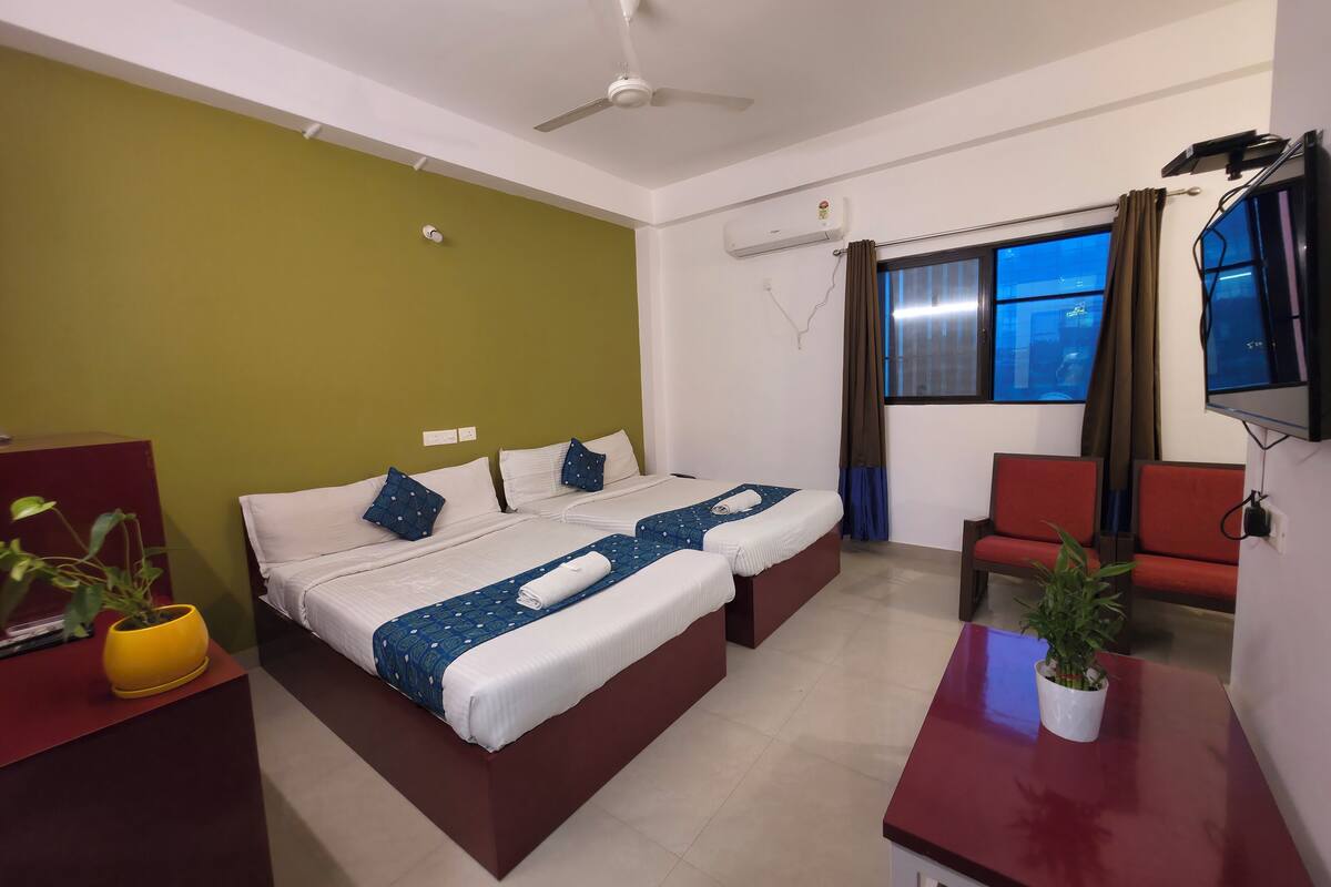Habitación de hotel con dos camas, un escritorio, una silla, un televisor y una ventana con cortinas.