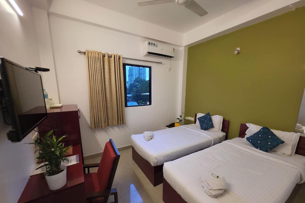 Habitación de hotel con dos camas, un escritorio con televisor, una silla, una planta en maceta y una ventana con cortinas.