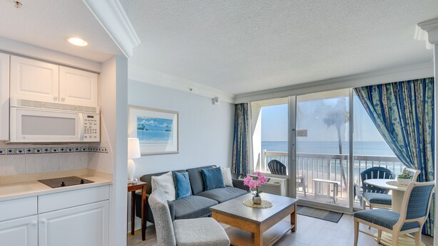 A modern living room with a sofa, chairs, a coffee table, and a kitchen area with a microwave. - Daytona Beach Studio Condo w/ Ocean Views! (Daytona Beach)