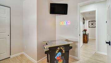 Une pièce avec un téléviseur à écran plat fixé au mur, un néon et une borne d’arcade Pac-Man.