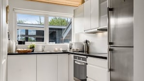 A modern kitchen with white cabinets, a stainless steel refrigerator, and a window with a view of a building outside.