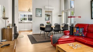 A modern living room with a red sofa, wooden coffee table, and a dining area with a red table and black chairs.
