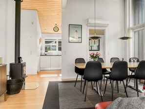 A modern kitchen with white cabinets, a wooden ceiling, and a dining area with a table and chairs.