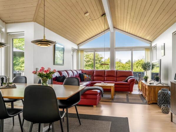A spacious living area with a red sofa, a dining table with chairs, and a television.