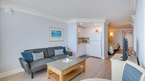 Een moderne woonkamer met een grijze bank, een houten salontafel en een kleine plant.