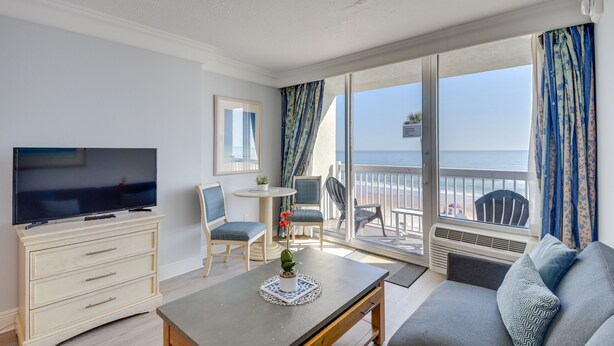 Een kamer met televisie, een bank, een eettafel en een balkon met uitzicht op zee.
