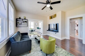 Ein modernes Wohnzimmer mit Sofa, einem grünen Sessel, Couchtisch, Wand-Fernseher und Deckenventilator.