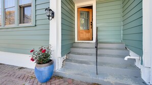 Una casa con fachada verde, puerta principal de madera y maceta azul con flores rojas.