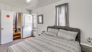 A bedroom with a bed, a nightstand, a mirror, a ceiling fan, and a door leading to a bathroom. - Harrisburg Home w/ Private Yard + Screened Porch! (Harrisburg)