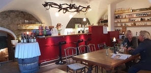A restaurant interior with a bar area, wooden tables, chairs, and a wine rack.