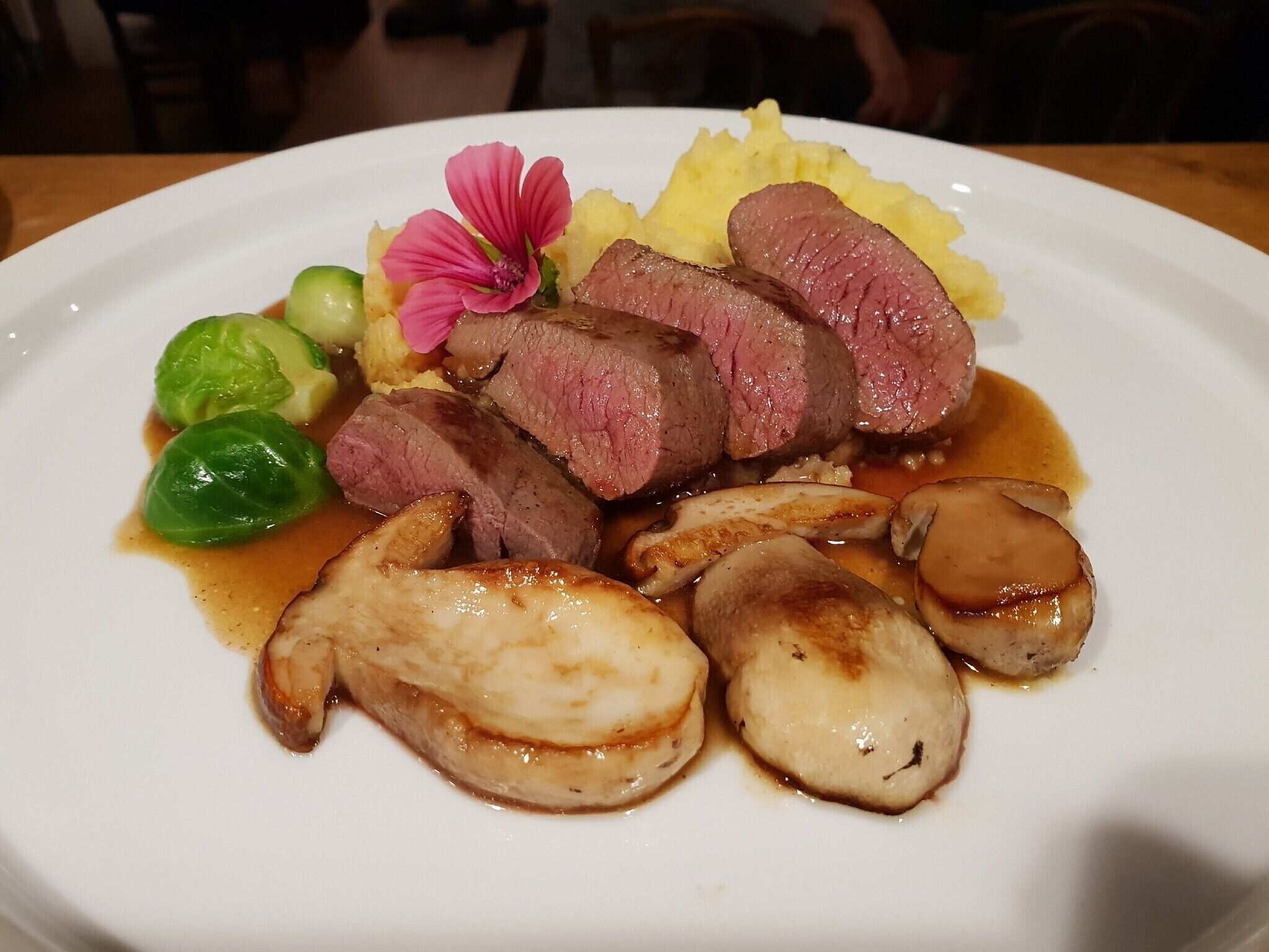 A plate of food with sliced meat, mushrooms, and Brussels sprouts.