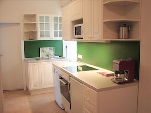 Une cuisine compacte avec des meubles blancs, un pare-feu vert, un four à micro-ondes, une machine à café et un lave-vaisselle.