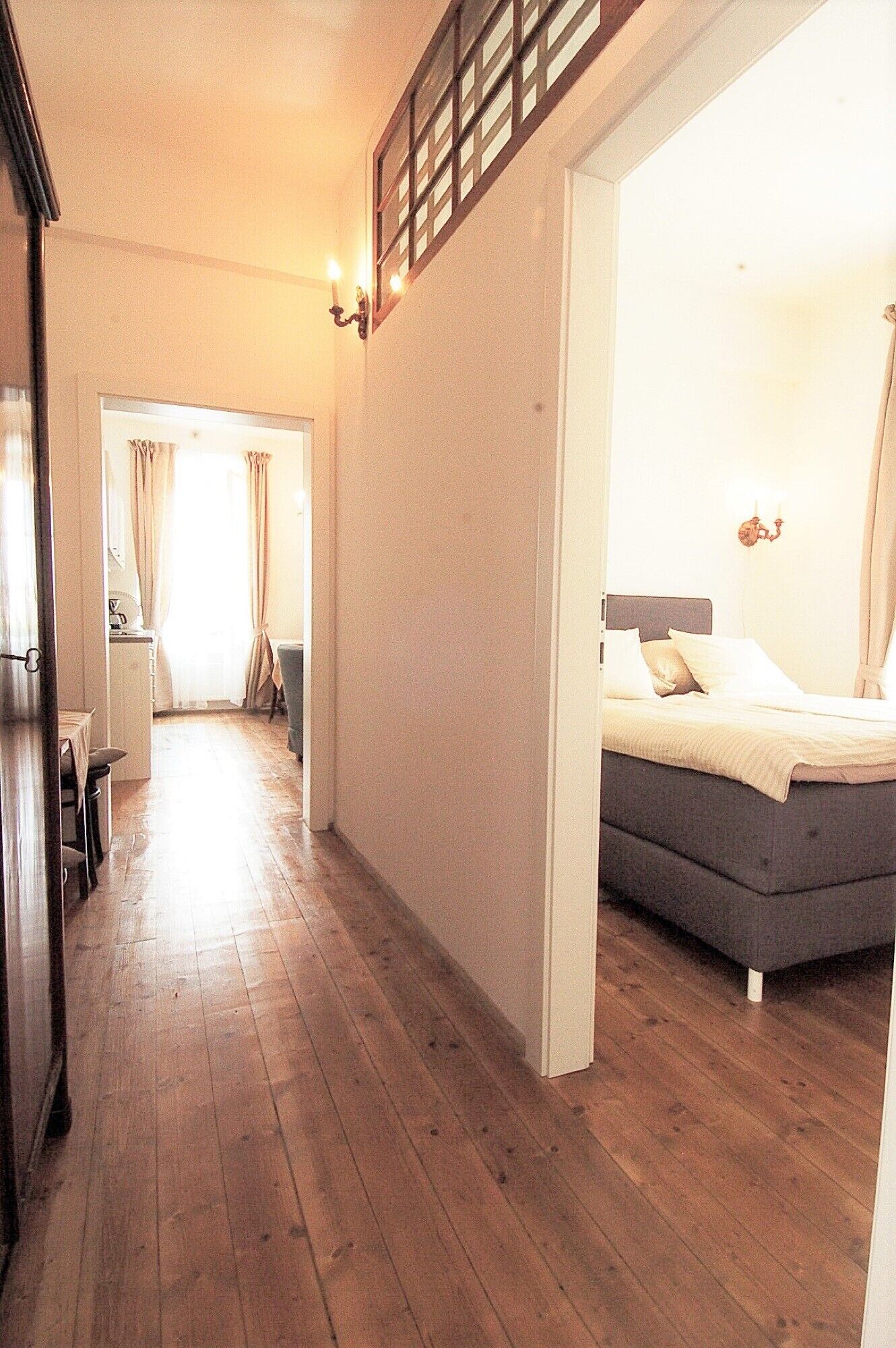 A hallway leading to a bedroom with a bed, a dining area, and a view of the outside.