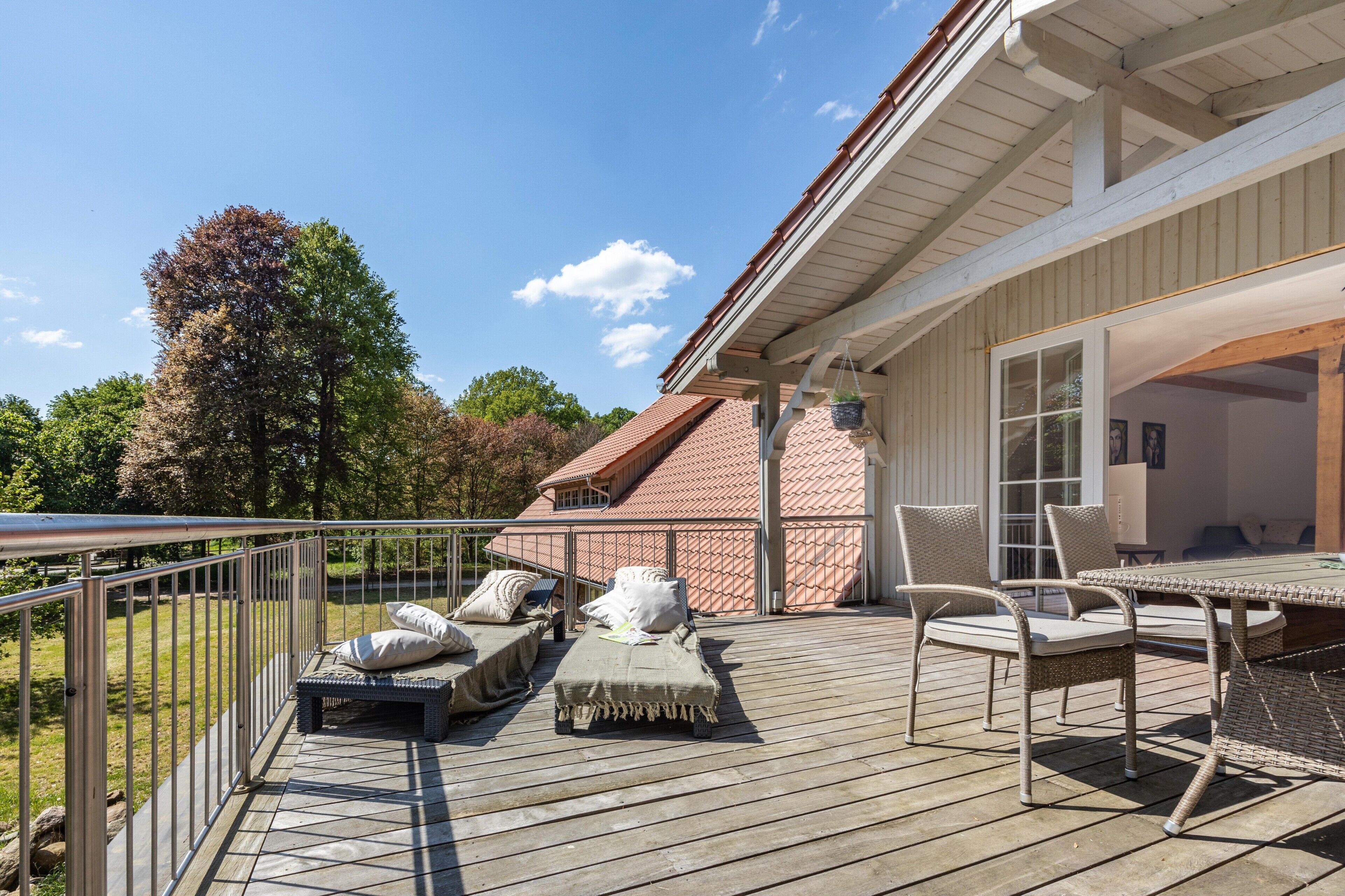 Una terraza con mobiliario exterior, una mesa y barandilla con vista a un jardín.