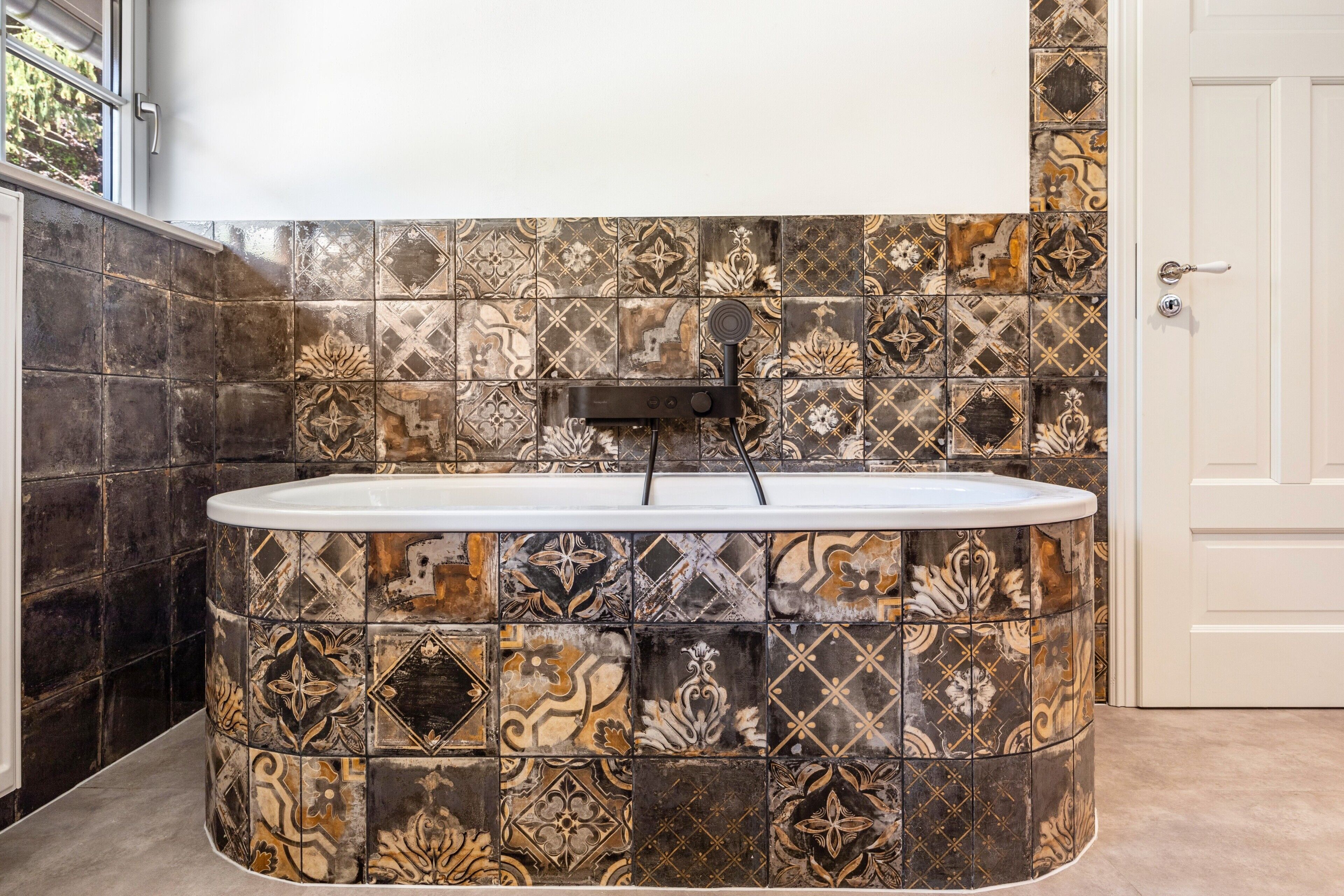 A bathtub with a showerhead in a corner, surrounded by patterned tiles.