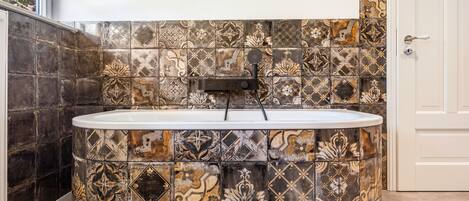 A bathtub with a showerhead in a corner, surrounded by patterned tiles.