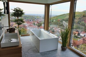 Une salle de bain moderne avec une grande baignoire, un lavabo et une vue sur la ville grâce à de grandes fenêtres.