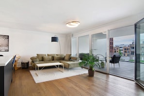 Un salon moderne avec un canapé d’angle, une petite table, une plante en pot et une vue sur la ville grâce à de grandes portes vitrées.