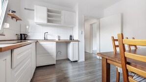 A modern kitchen with white cabinetry, a wooden countertop, and a dining area with a wooden table and chairs. - Inn 'Haus Am Garten' with Private Terrace, Garden and Balcony (Alfeld (Leine))