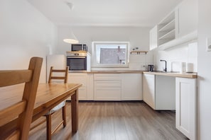 A compact kitchen with white cabinetry, a wooden dining table, and a window providing natural light.