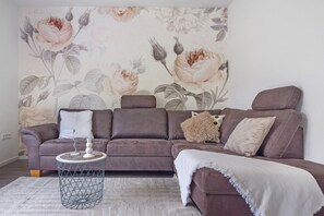 A living room with a sofa, a side table, and a floral wallpaper.
