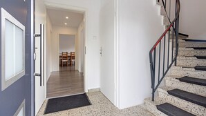 A staircase with a metal handrail, a door leading to a hallway, and a dining area with chairs. - Inn 'Haus Am Garten' with Private Terrace, Garden and Balcony (Alfeld (Leine))