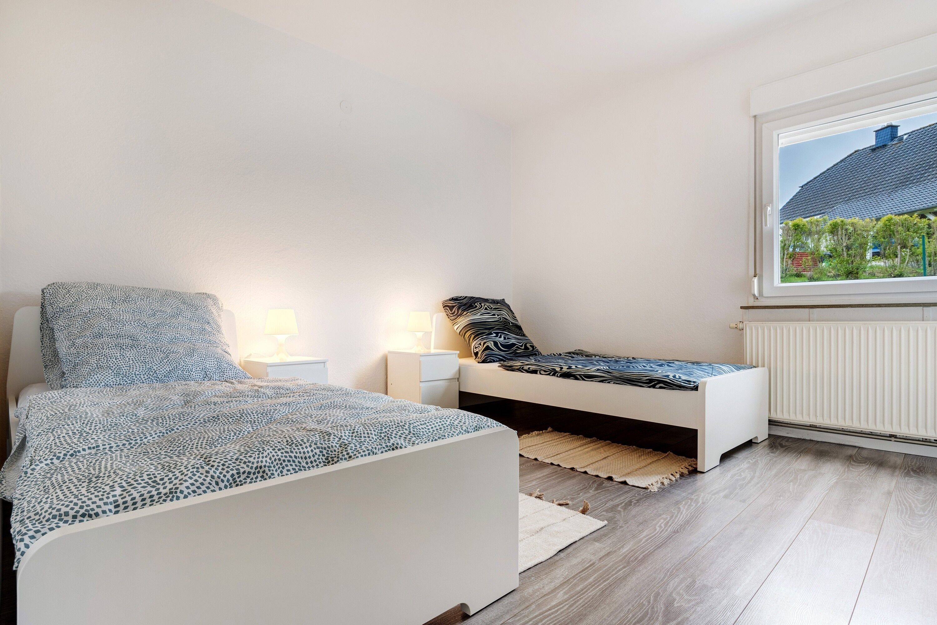 Une chambre à coucher avec un lit, des tables de chevet, une fenêtre donnant sur un paysage agréable et un radiateur.