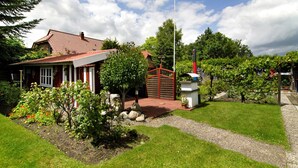 A house with a red roof, a garden with various plants, a red gate, and a white building with a red roof. - Apartment 'Ferienhaus Gerda Wohnung 2' with Private Terrace, Private Garden and Wi-Fi (Ochtersum)