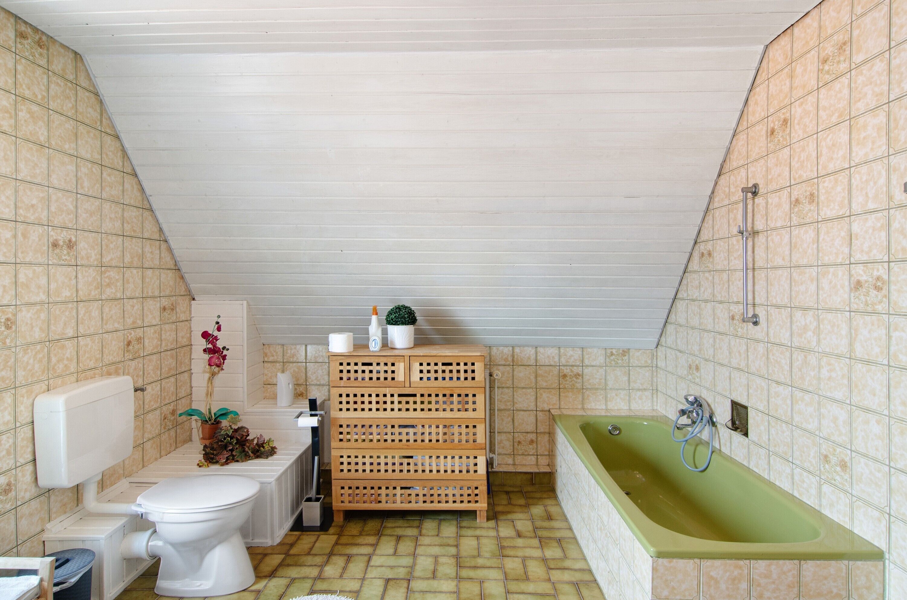 Ein Badezimmer mit Toilette, Waschbecken, einer Holzaufbewahrung und einer grünen Badewanne.
