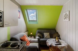 Et lille, hyggeligt værelse med tekøkken, et vindue, en sofa og et bord med fjernbetjening.