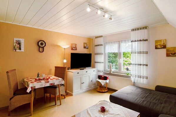 A cozy room with a dining table, chairs, a sofa, a TV, and a window with curtains. - Apartment 'Ferienhaus Gerda Wohnung 1' with Private Terrace, Private Garden and Wi-Fi (Ochtersum)