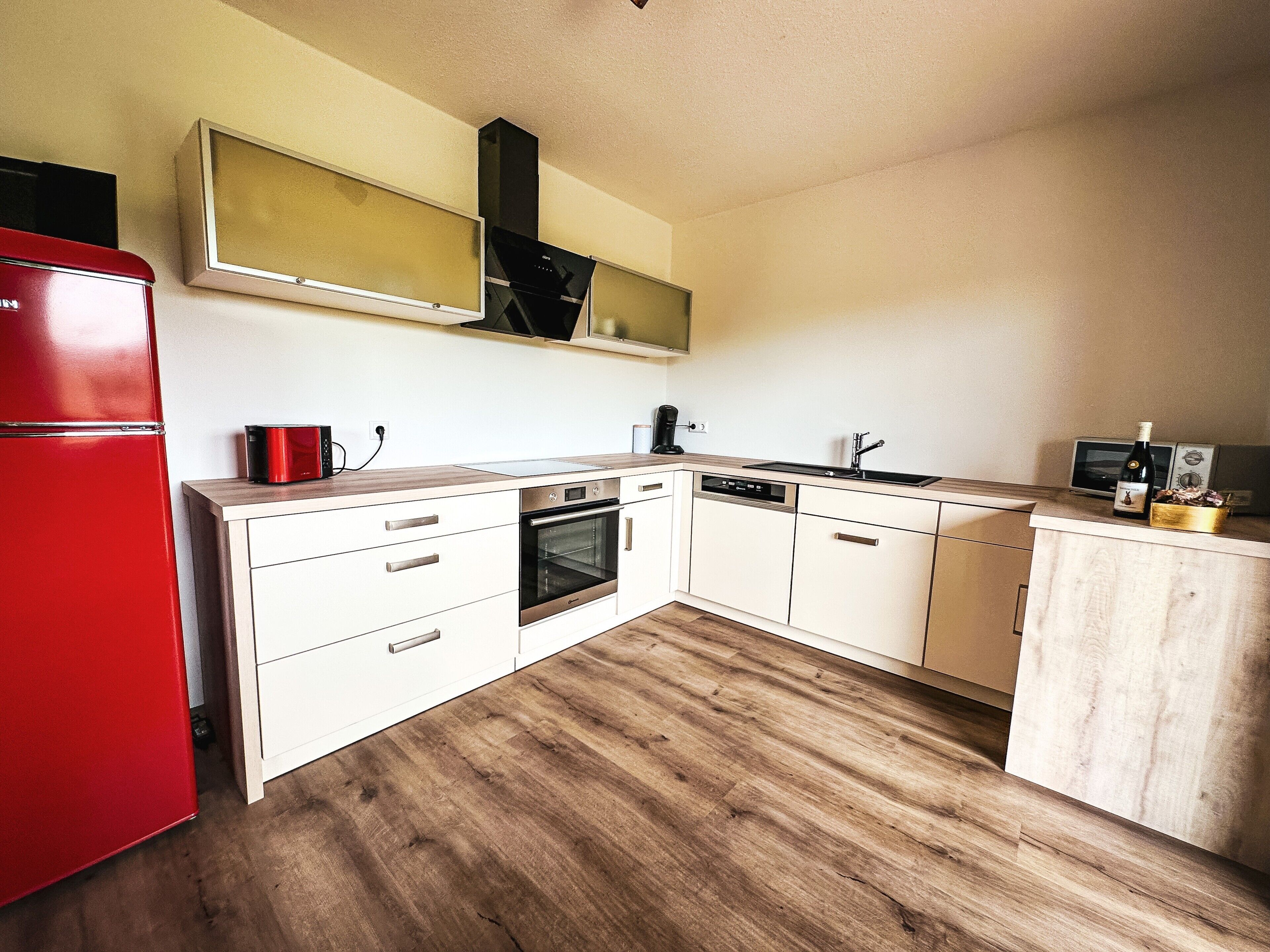 Eine kompakte Küche mit rotem Kühlschrank, eingebautem Ofen, Geschirrspüler und Mikrowelle.