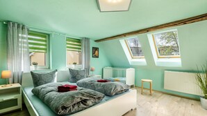 A bedroom with a bed, two windows, a radiator, a small table, and a plant. - Holiday Home 'Ferienhaus Fichtelberg' with Mountain View, Private Terrace and Wi-Fi (Oberwiesenthal)