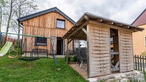 A wooden cabin with a swing set and a small shed. - Holiday Home 'Ferienhaus Fichtelberg' with Mountain View, Private Terrace and Wi-Fi (Oberwiesenthal)