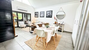 Un espace repas moderne avec une table ronde, des chaises blanches et un grand miroir au mur.